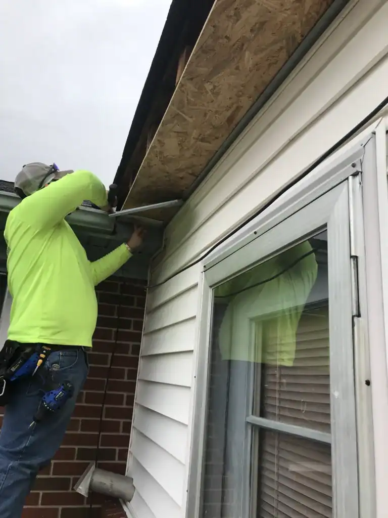 Fascia contractor installing vinyl soffit plastic panels into the facade ceiling of a. house by an employee
