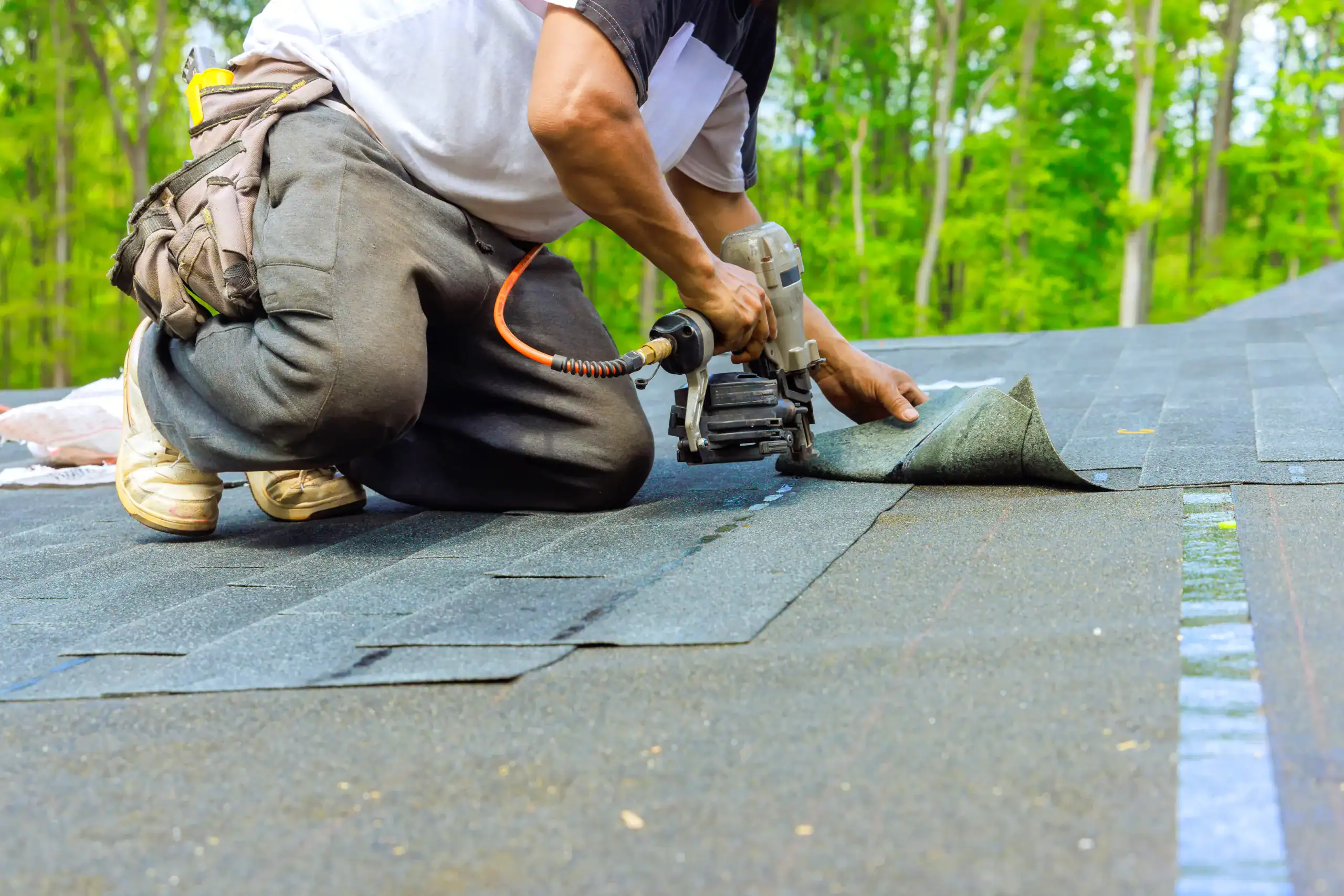 As roofer installed new bitumen shingles on his roof, he used an air pneumatic nail gun to secure them a roof