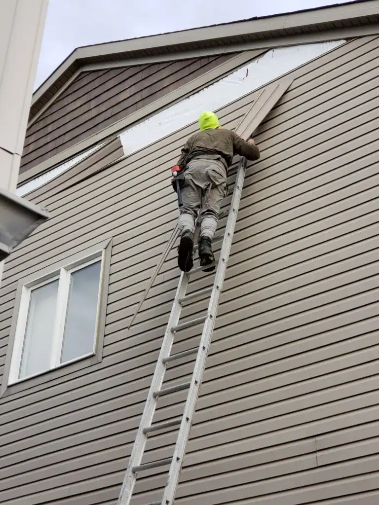 Man on the exterior of the home climbing a later and doing home siding repairs and renovations