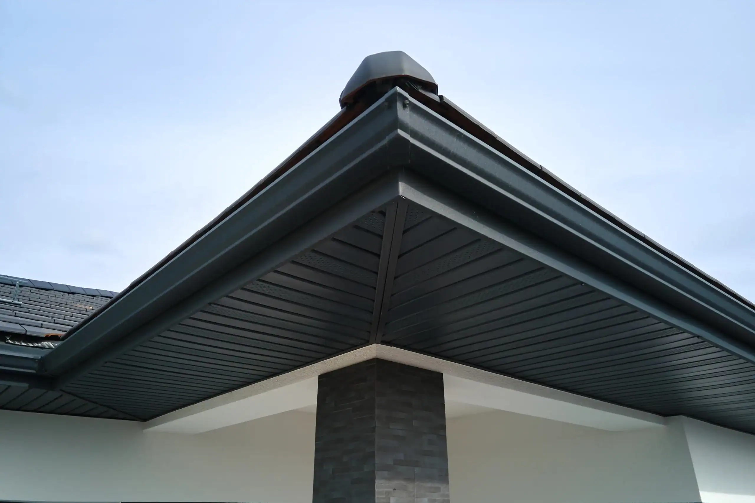 House corner with brown metal planks siding and roof with steel gutter rain system. Roofing, construction, drainage pipes installation.