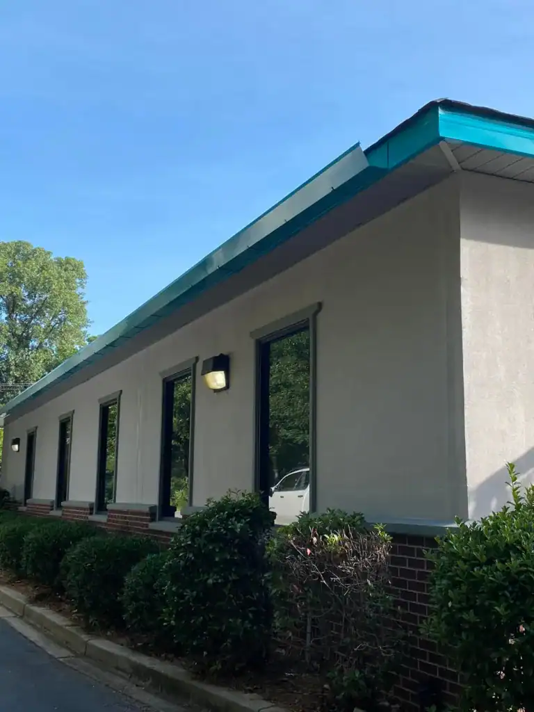 Exterior view of a commercial building with large windows and a blue metal roof.