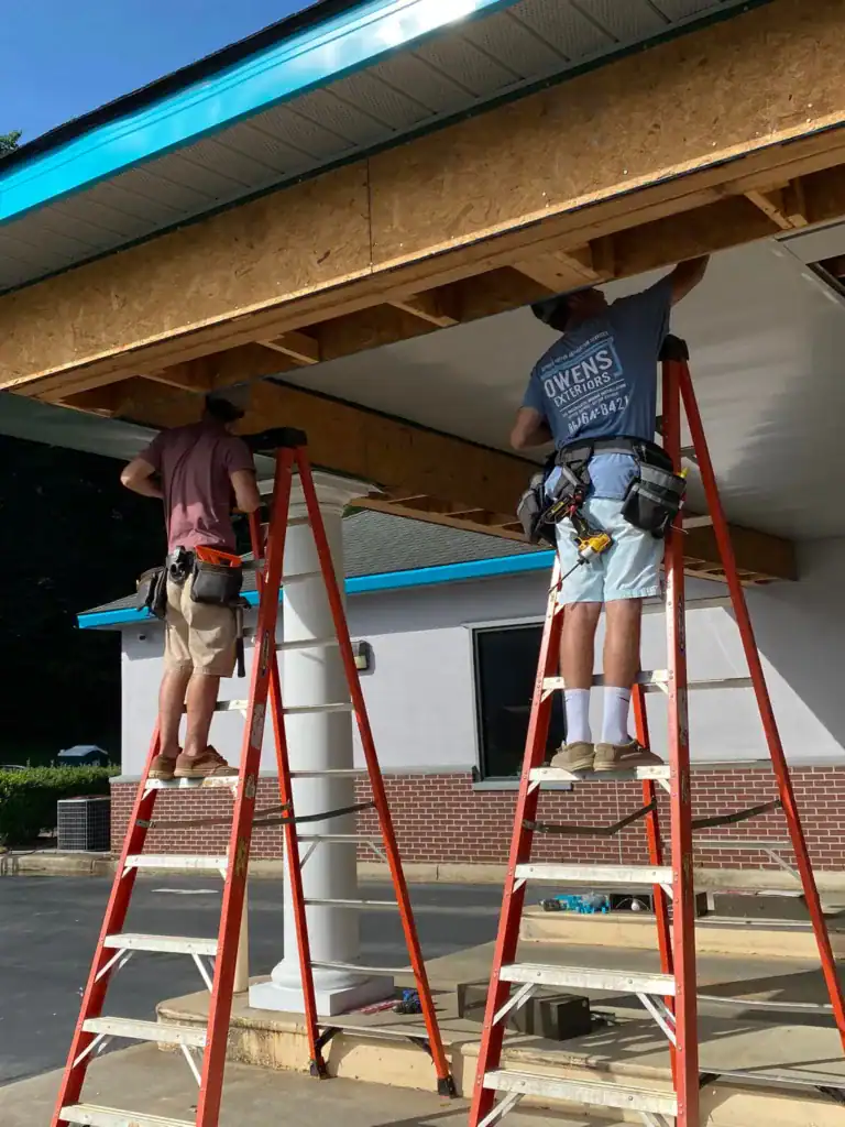 Roof repair with workers on ladders under the eaves.