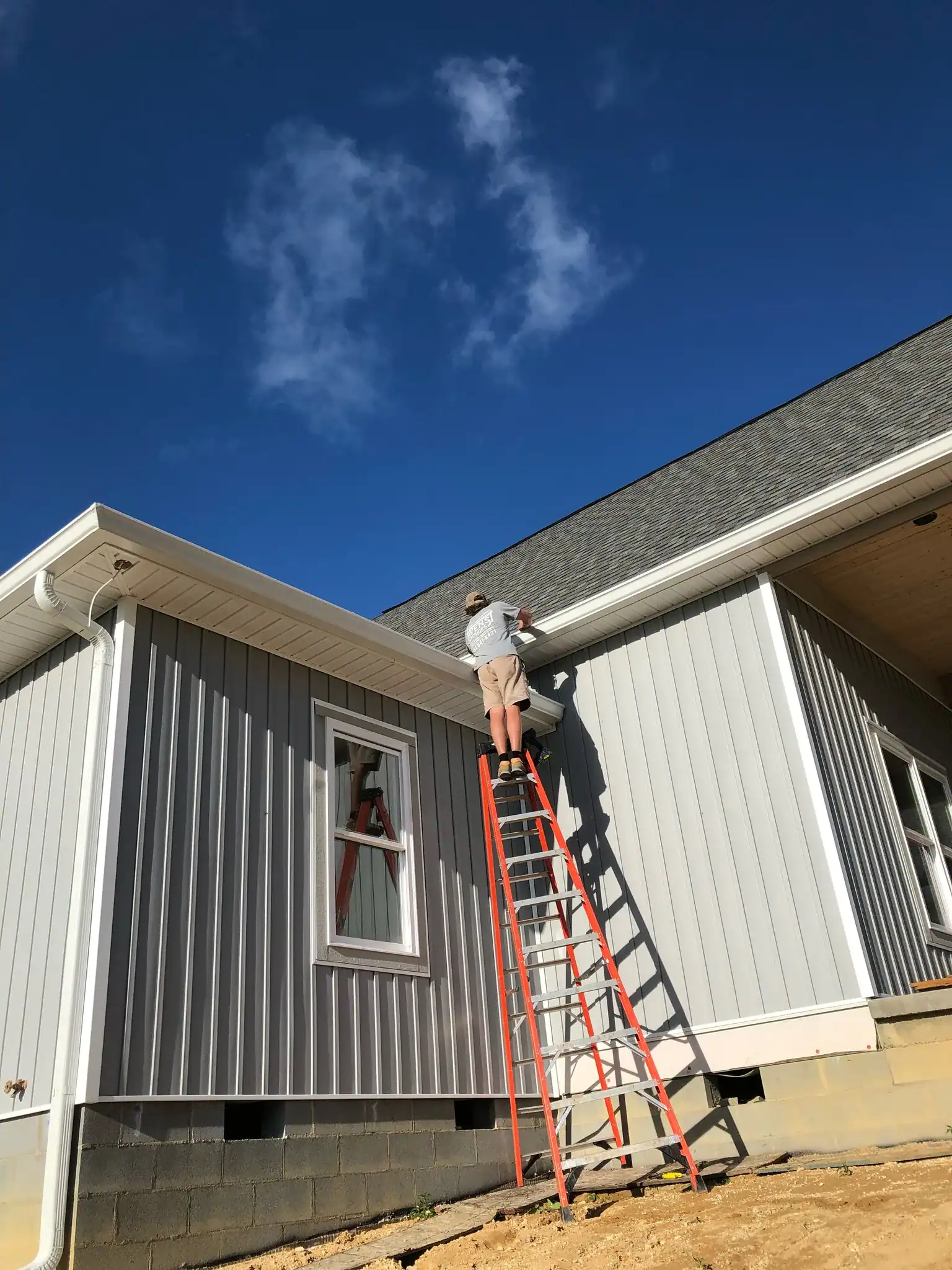 House painter applying exterior paint on a modern home with ladder.