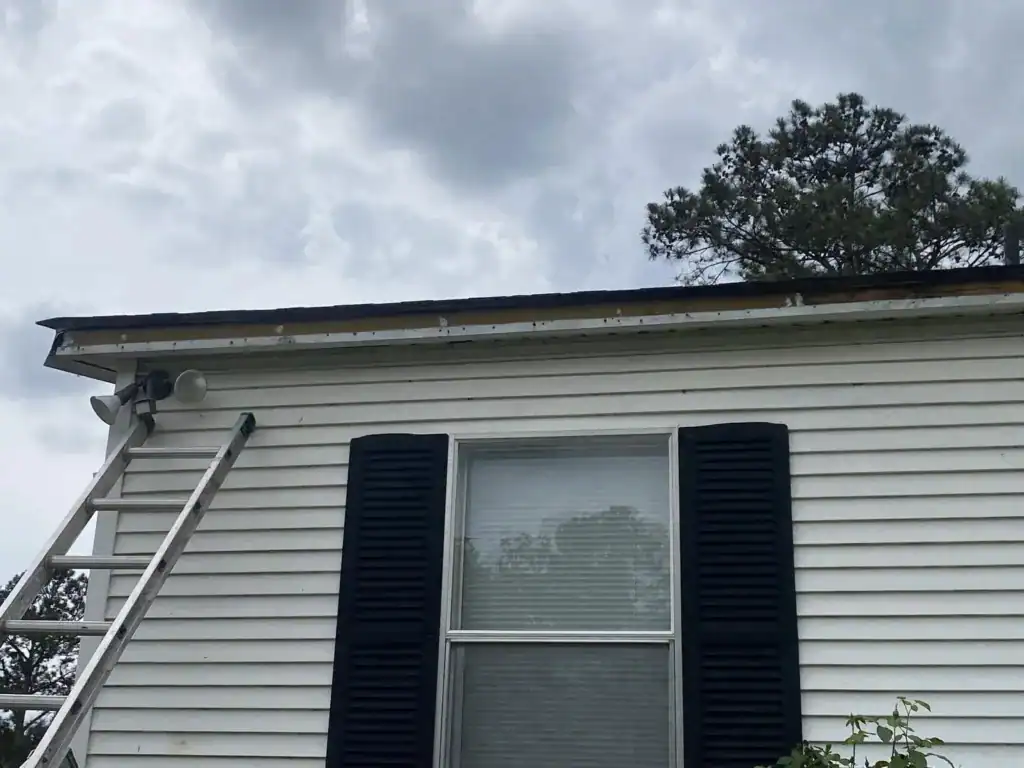 House exterior with white siding, black shutters, and a window, showing a cloudy sky and trees in th.